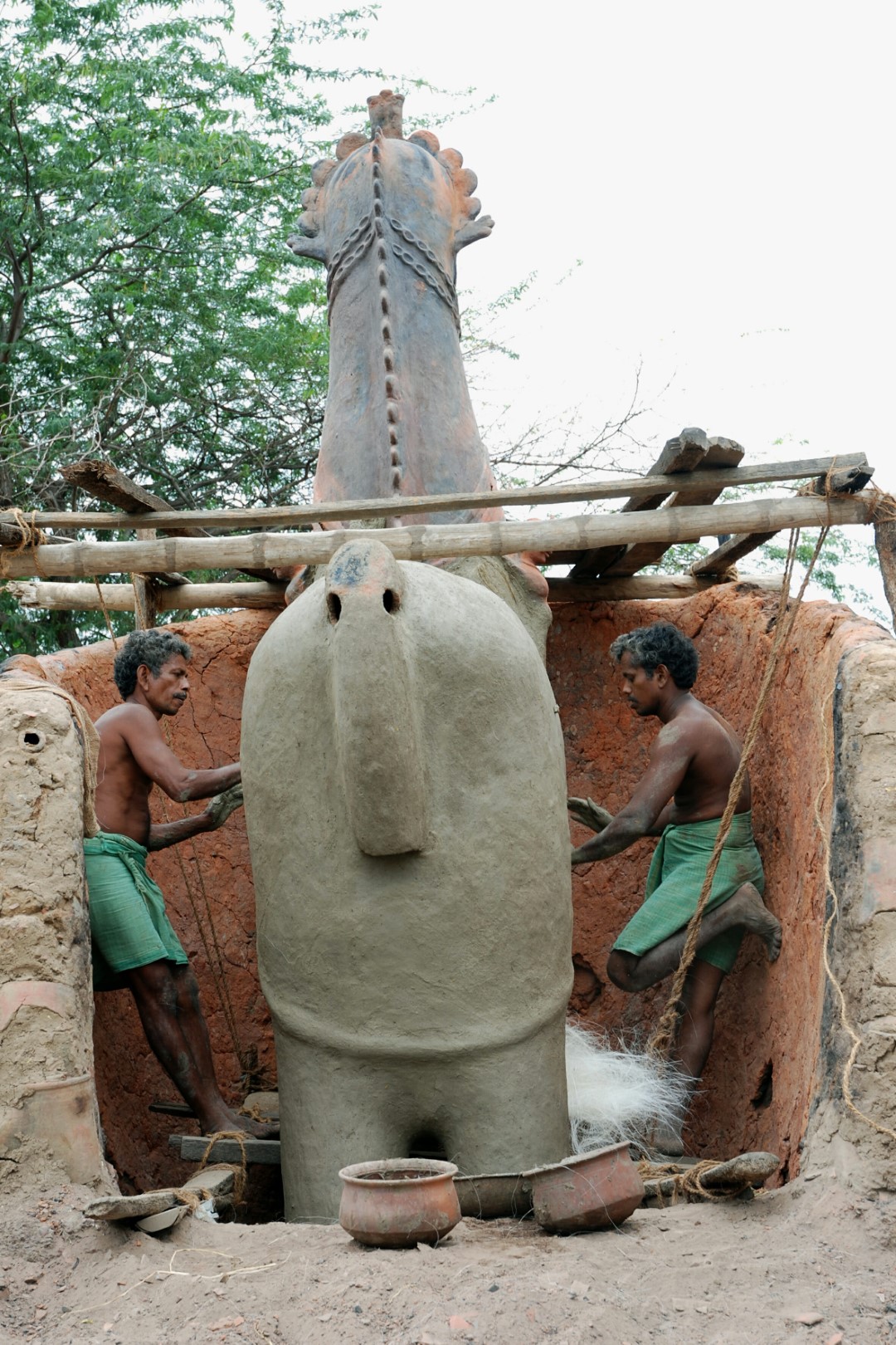 <span style="font-weight:normal;">After baking and before the first coat of white-lime is applied, this gigantic horse is given one last caress: its body and legs are covered with a mixture of wet mud and banana fibre, reinforcing it for its journey to the shrine using long bamboo poles tied to its haunches.</span>