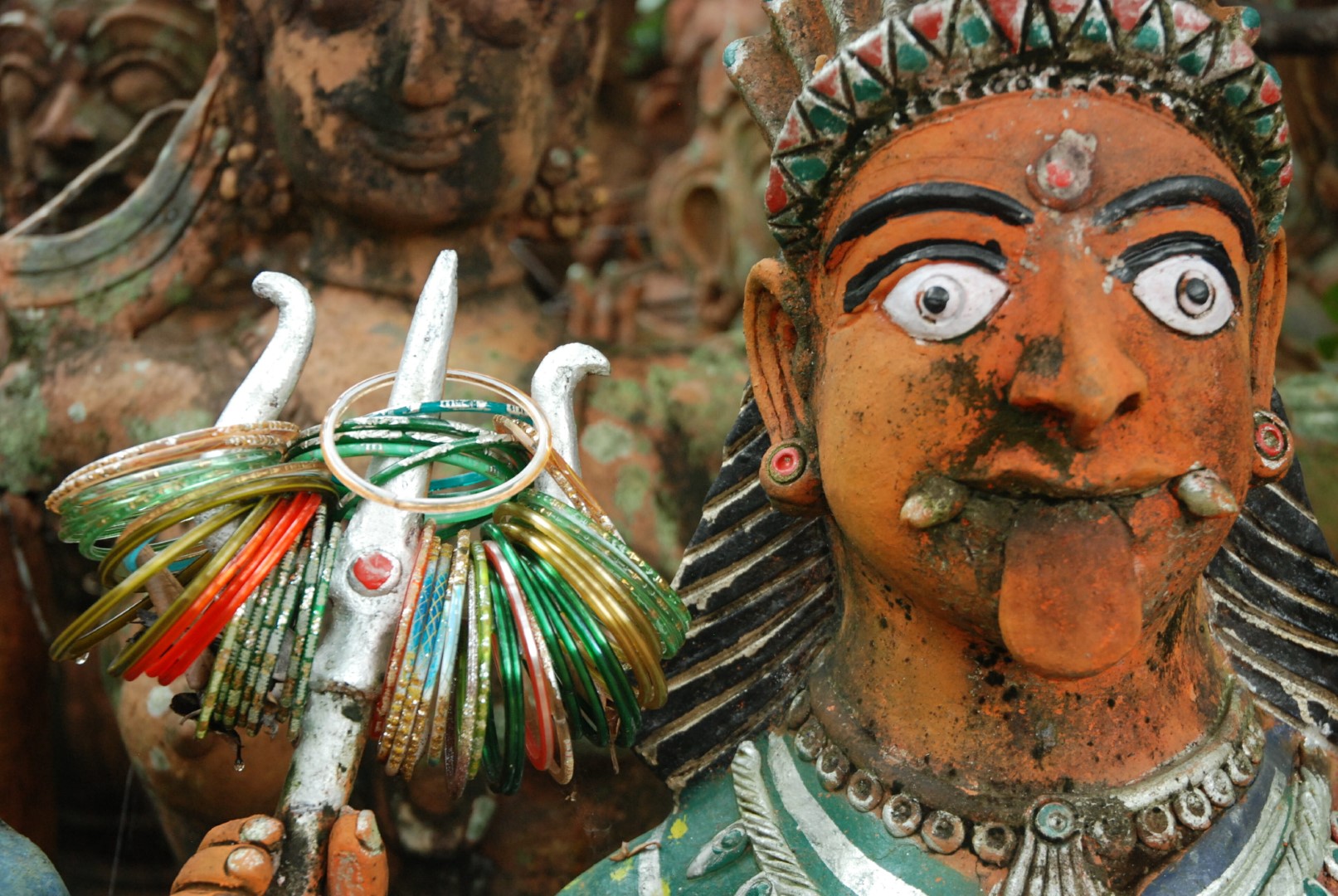<span style="font-weight:normal;">A "portrait" of Kaliyamman, with a Mona Lisa smile, fangs and her red tongue sticking out - telling attributes of her ambivalent nature. On her trident are glass bangles given as offerings by devotees - gifts to please her, appease her wrath and plead for fertility for women, and health, healing and protection of children.</span>